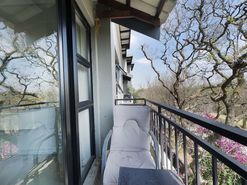A balcony featuring a metal balustrade and sliding glass door access, offering an elevated view of the surrounding trees and garden.