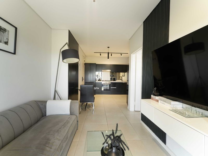 Modern open-plan living area featuring sleek black cabinetry, integrated kitchen appliances, contemporary track lighting, and stylish slatted wall accents.