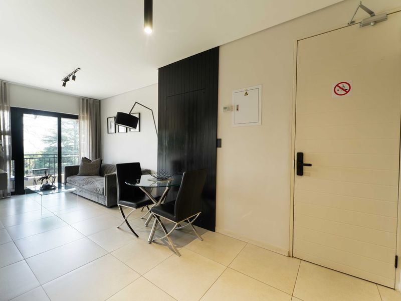 Modern open-plan living area featuring large format floor tiles, track lighting, and a sliding glass door leading to an outdoor balcony.
