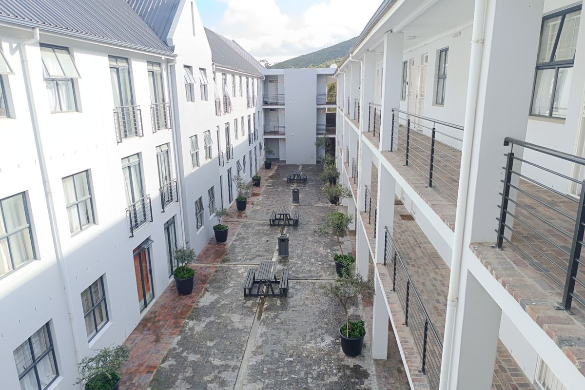 An elevated view of an apartment complex courtyard featuring brick paving, covered walkways, and multi-story residential units with metal railings.