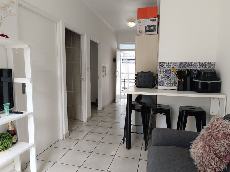 Open plan living area featuring tiled flooring, a breakfast bar with decorative backsplash, and access to internal rooms and the exterior balcony.