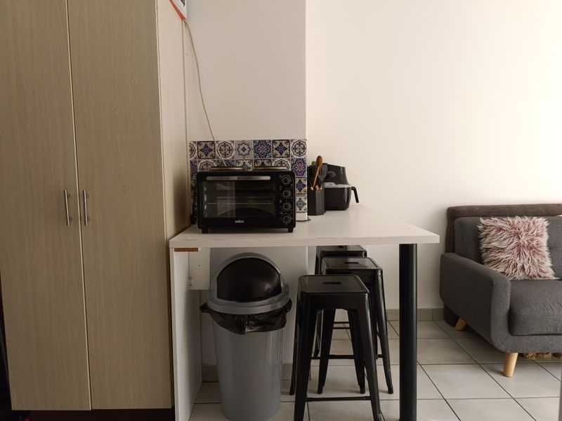 A compact kitchen area featuring built-in cabinetry, a decorative tiled backsplash, and tiled flooring, providing a functional prep space within the apartment.
