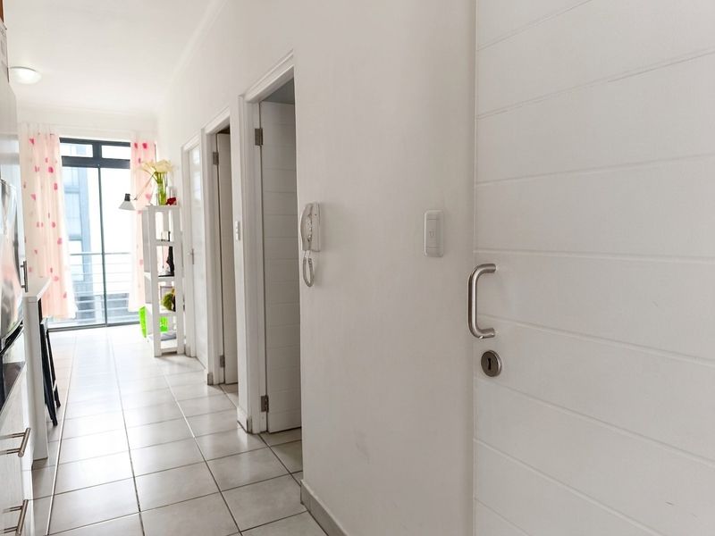 A bright, tiled hallway featuring an intercom system and access to multiple rooms, leading towards a balcony area.