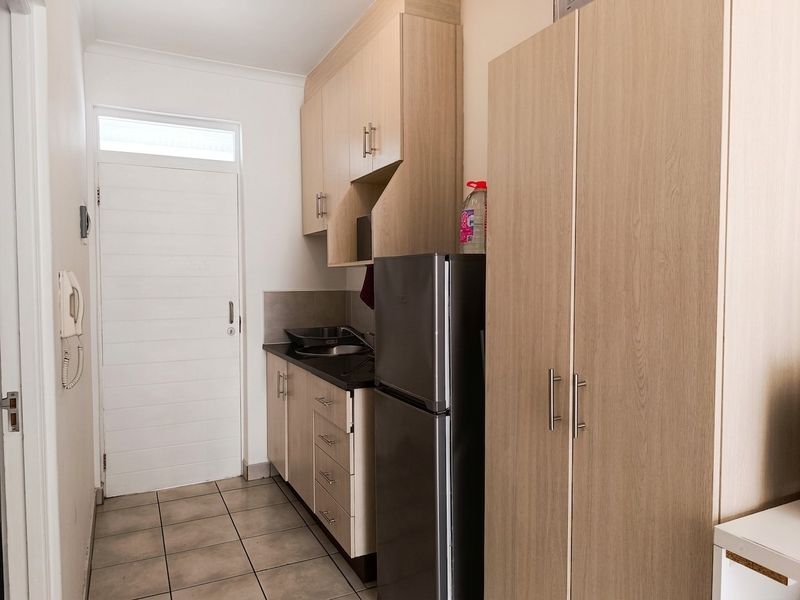Compact kitchen featuring light wood-finish cabinetry, laminate countertops, a stainless steel sink, and tiled flooring, providing a functional and efficient workspace.