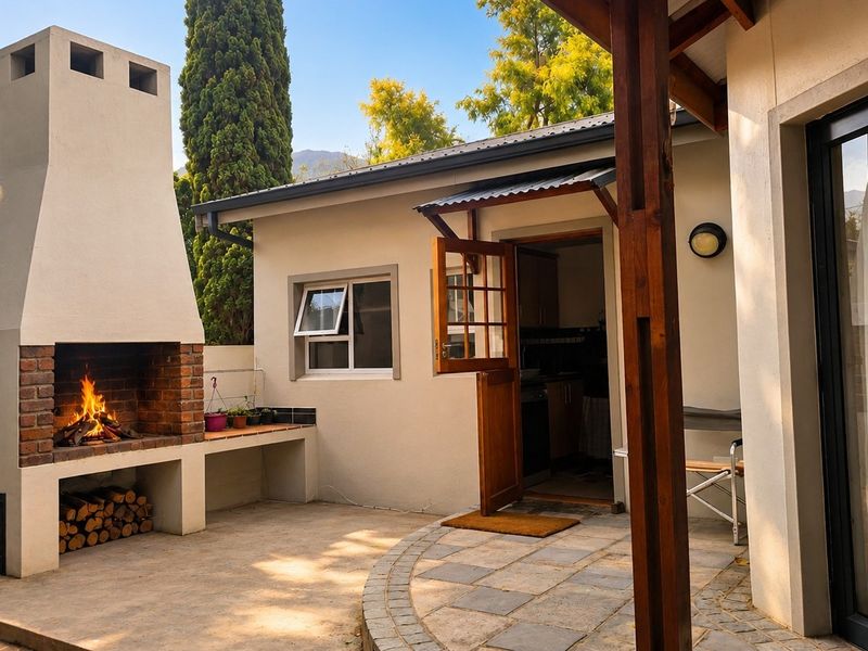 A well-maintained outdoor patio area featuring a large built-in brick fireplace, concrete flooring, and direct access to the home through a timber door.