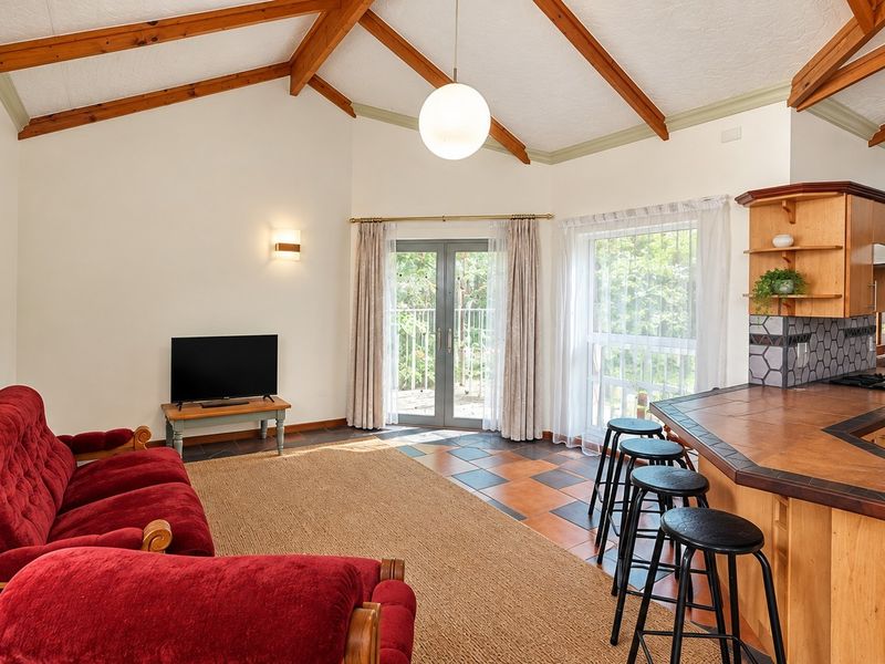 Open-plan living and kitchen area featuring vaulted ceilings with exposed timber beams, tiled flooring, and direct access to the outdoors through glass doors.