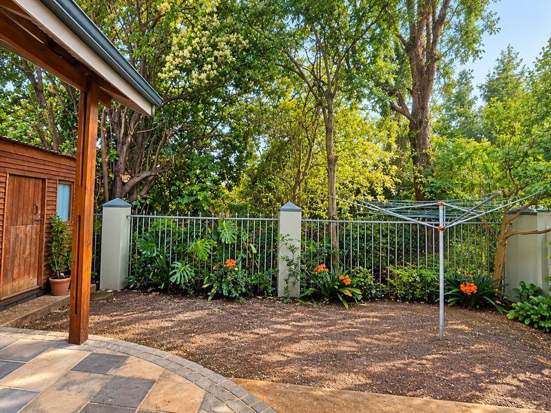 A private rear garden area featuring a paved patio, a timber storage shed, and secure metal perimeter fencing with established trees.