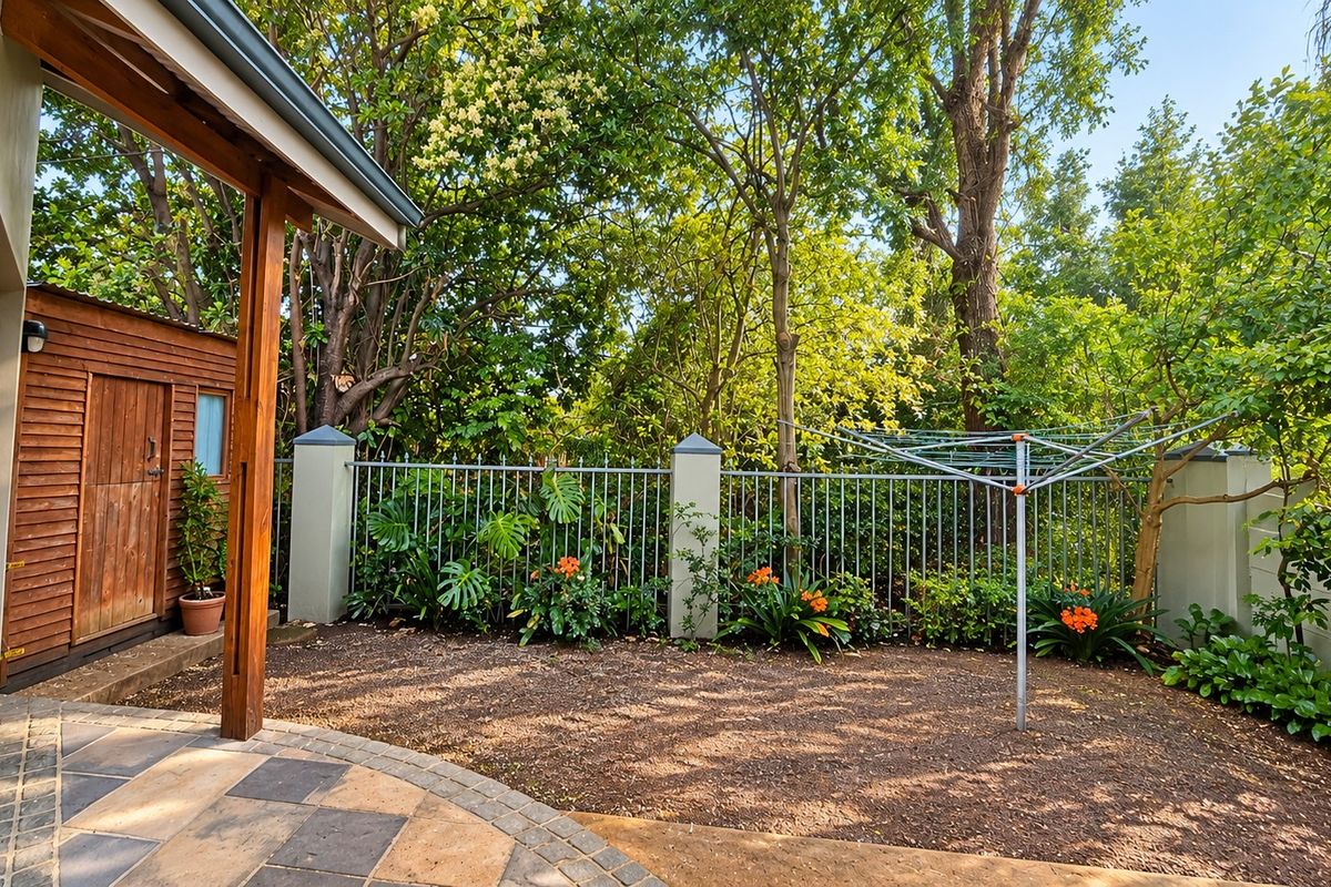 A private rear garden area featuring a paved patio, a timber storage shed, and secure metal perimeter fencing with established trees.