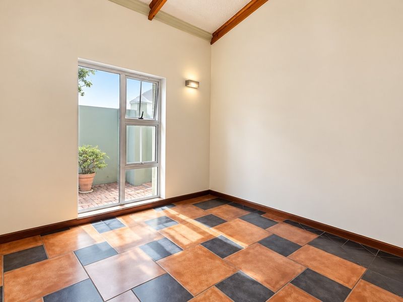 An empty living area featuring a vaulted ceiling with exposed timber beams, tiled flooring, and a large window providing natural light.