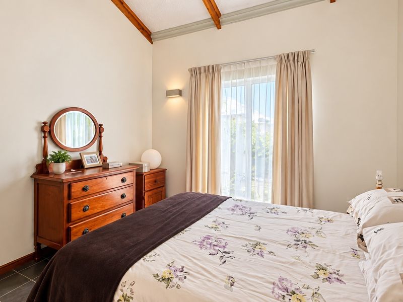 A bright bedroom featuring a vaulted ceiling with exposed timber beams, tiled flooring, and a sliding glass door providing natural light.