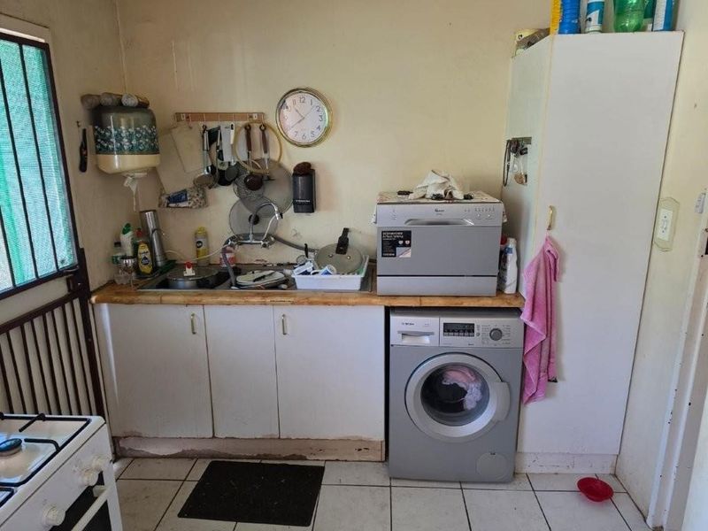 A functional laundry area featuring tiled flooring, built-in cabinetry, a stainless steel sink, and dedicated space for a washing machine.