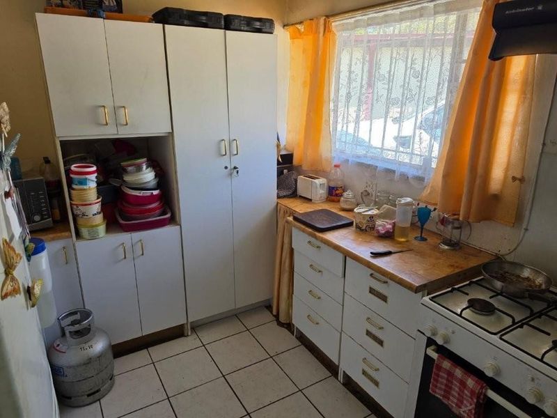 A compact kitchen featuring white built-in cabinetry, a gas stove with extractor fan, and tiled flooring, offering potential for a modern renovation.