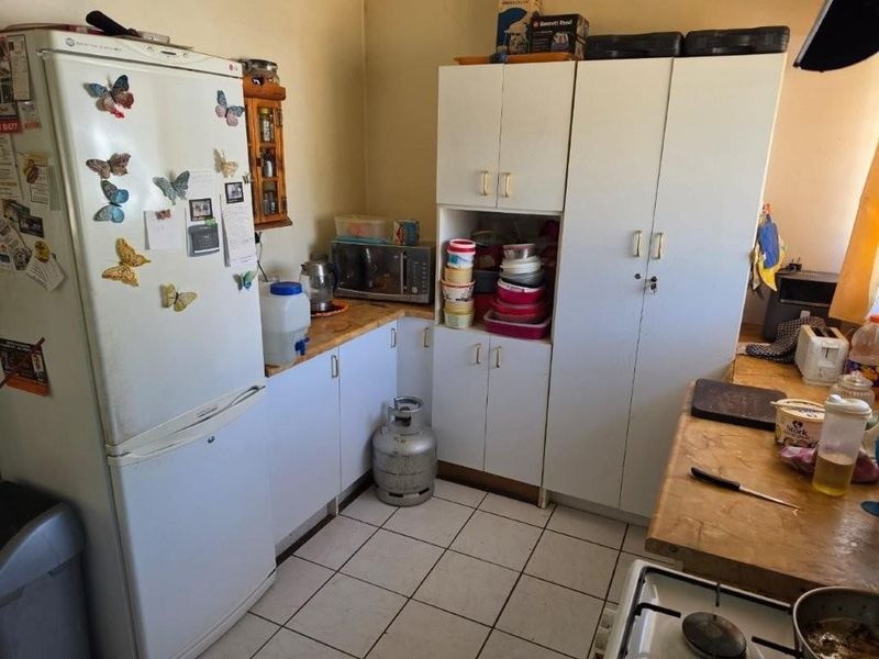 A functional kitchen featuring white built-in cabinetry, tiled flooring, and a gas hob, offering a practical layout with potential for modern updates.