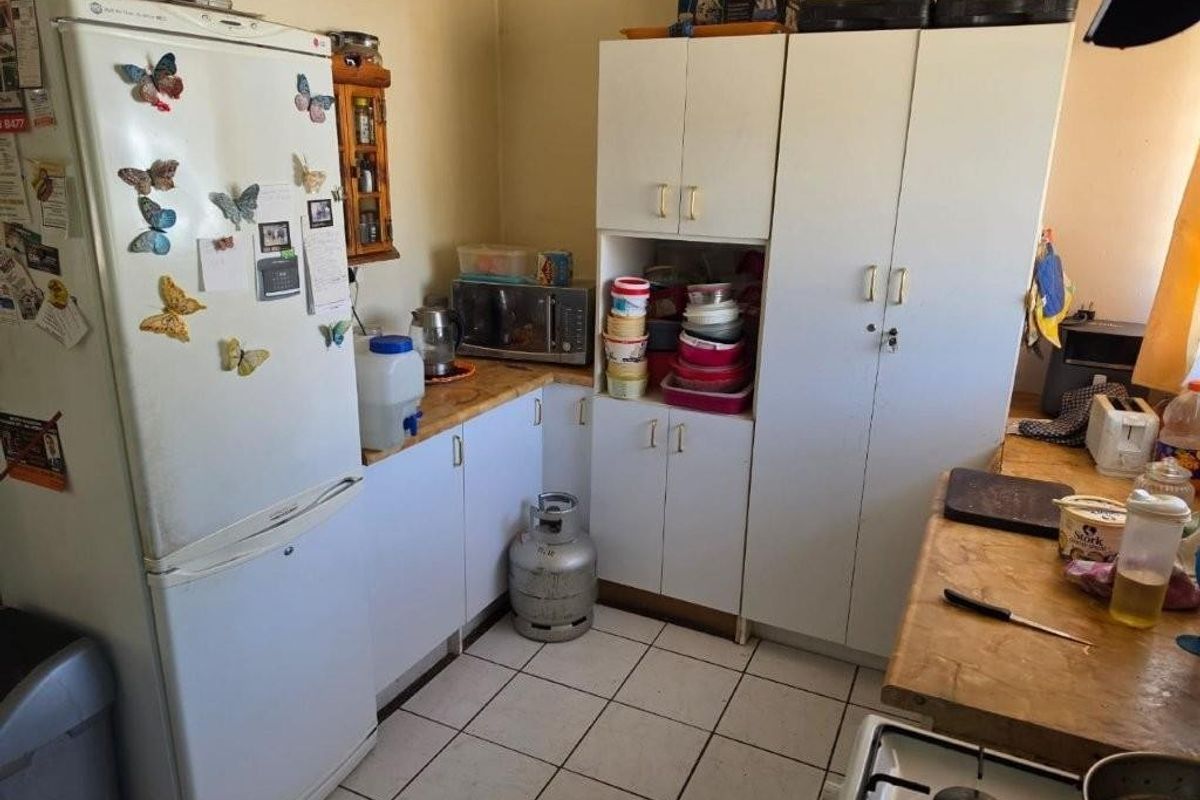A functional kitchen featuring white built-in cabinetry, tiled flooring, and a gas hob, offering a practical layout with potential for modern updates.