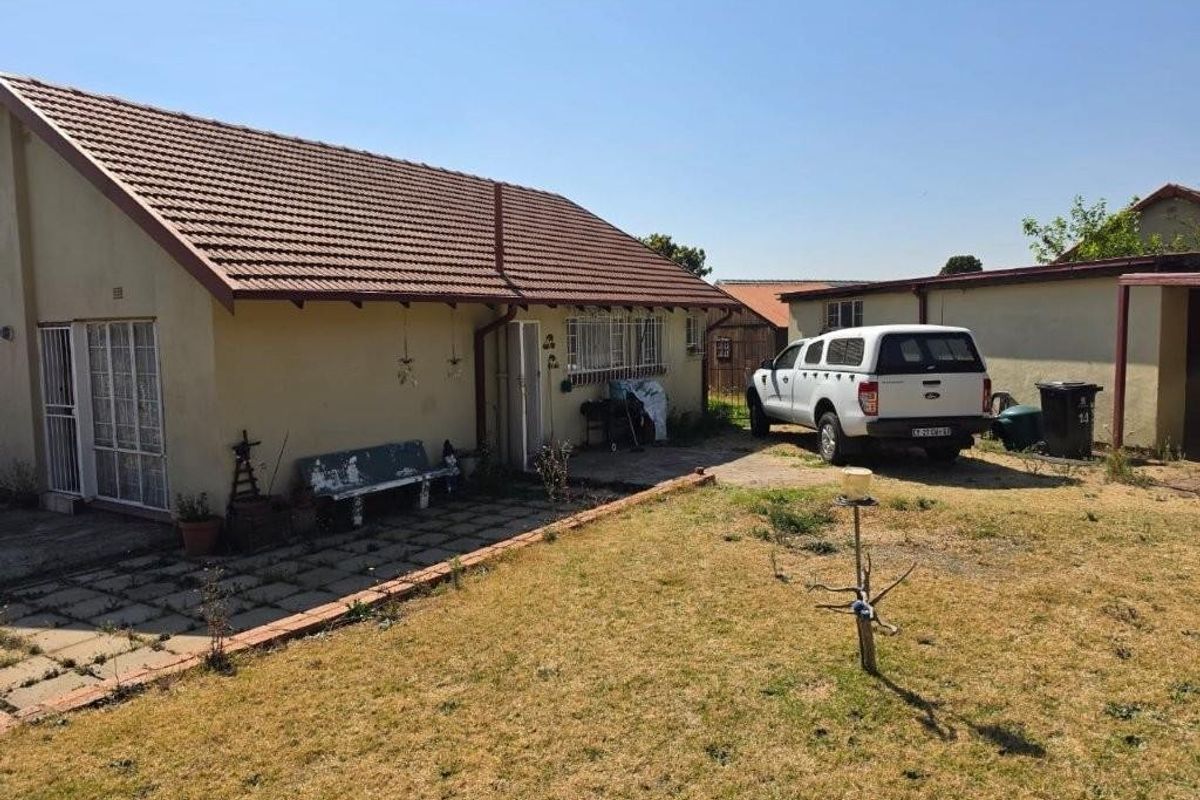 Rear view of the property featuring a tiled roof, paved patio area, and a garden space with established boundary lines.