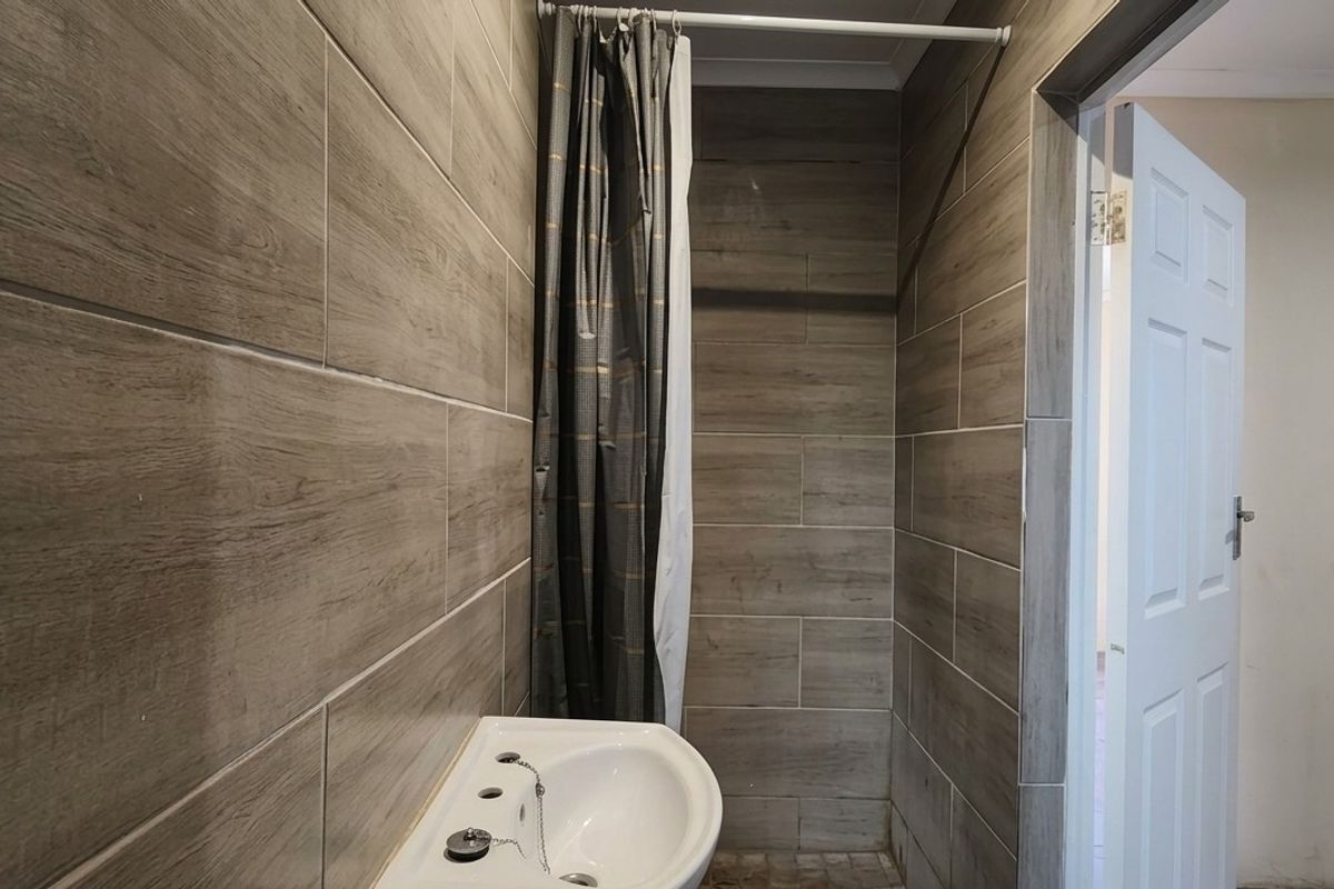 A compact bathroom featuring wood-look wall tiles, a wall-mounted basin, and a shower area with a curtain.