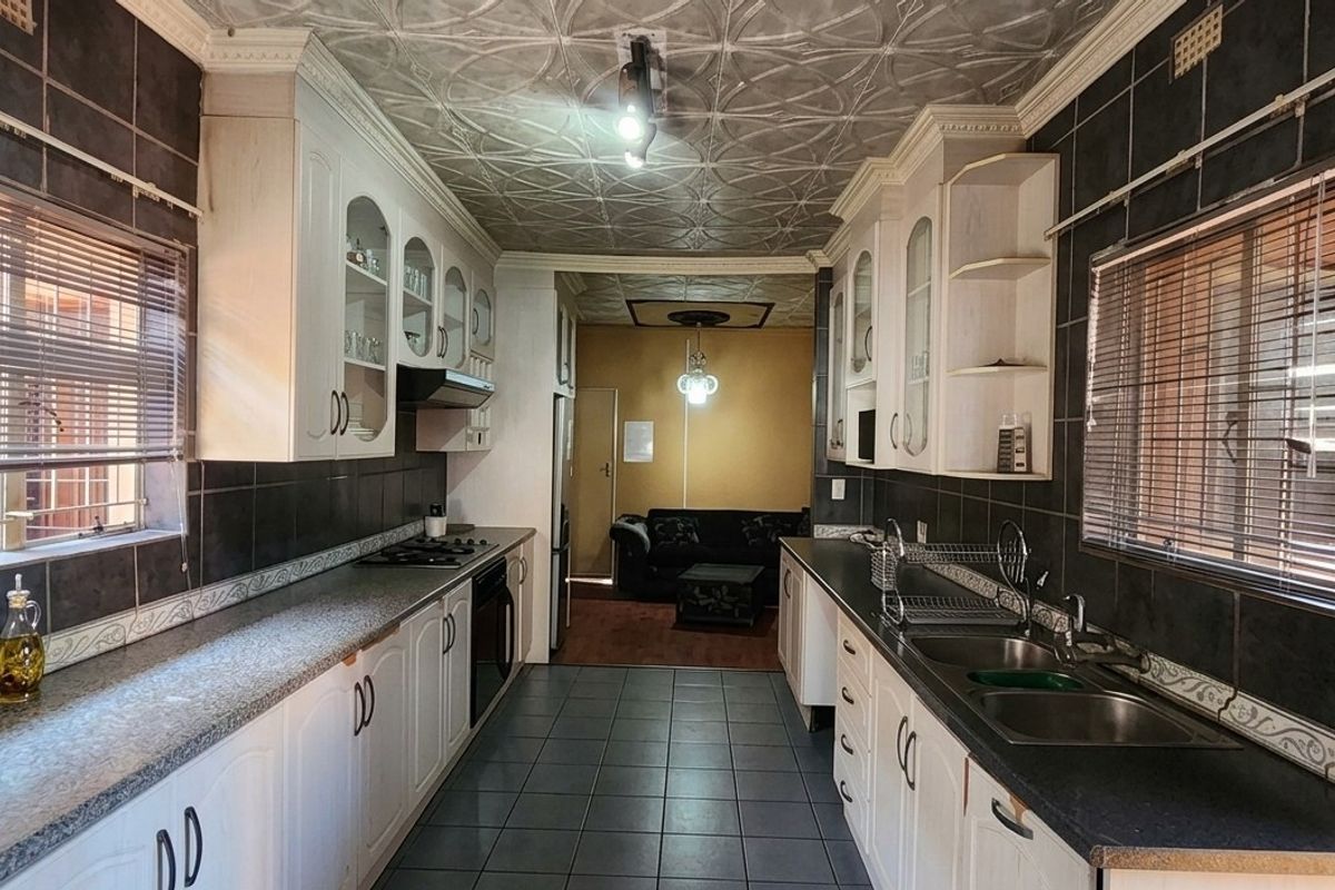 A functional galley-style kitchen featuring built-in cabinetry, dark tiled backsplash, double basin sink, and integrated cooking appliances with decorative ceiling detailing.
