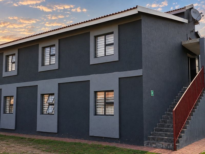A well-maintained two-story commercial building featuring a dark grey facade, external staircase, and aluminium window frames set against a sunset sky.