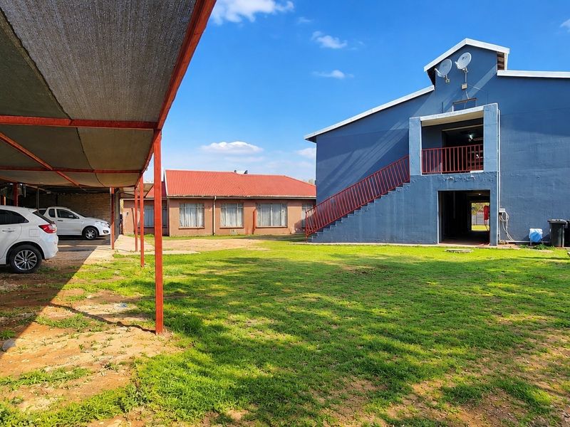 Rear view of the commercial property featuring a large lawn, covered carport parking, and an external staircase leading to the upper level.