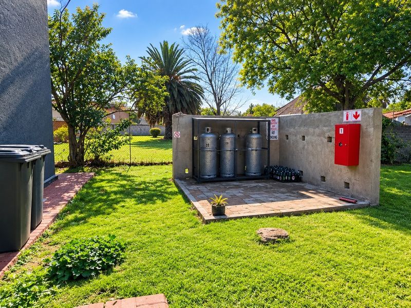 Outdoor utility area featuring a secure gas cylinder storage cage, fire extinguisher station, and paved flooring set within a landscaped garden.