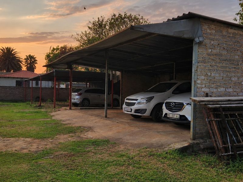 Open-sided commercial garage structure with exposed brick walls and corrugated metal roofing, providing covered parking space on a concrete slab.