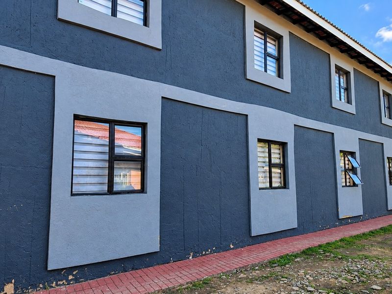 Side view of a two-story commercial building featuring dark grey textured walls, contrasting light grey window surrounds, and a paved ground-level walkway.