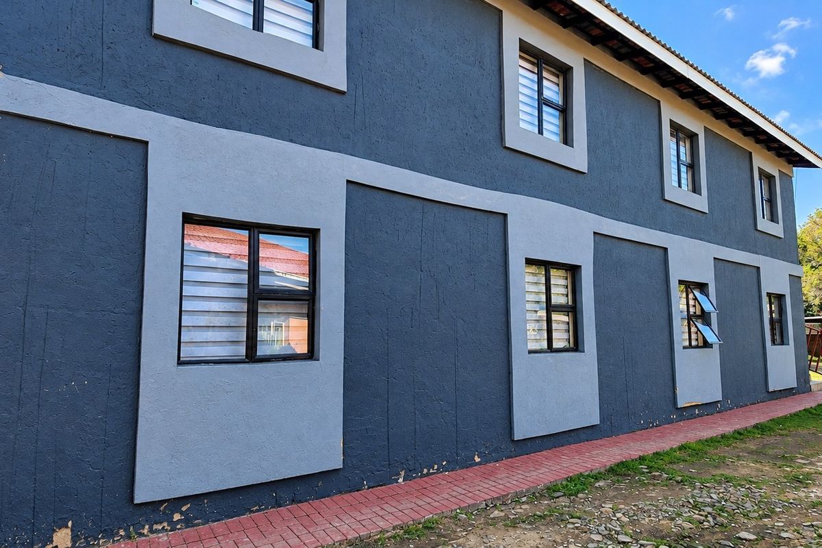 Side view of a two-story commercial building featuring dark grey textured walls, contrasting light grey window surrounds, and a paved ground-level walkway.