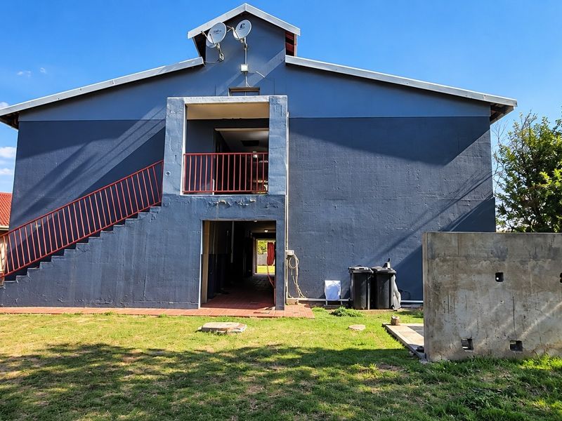 Rear view of a multi-story commercial building featuring an external metal staircase, blue painted facade, and a concrete retaining wall in the garden area.