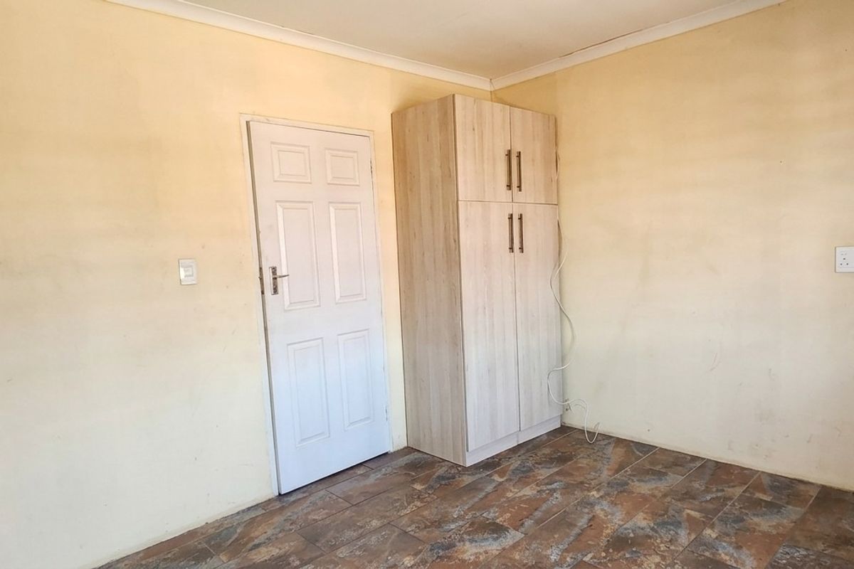 A vacant bedroom featuring tiled flooring, a built-in cupboard, and neutral wall finishes, offering a blank canvas for potential updates.