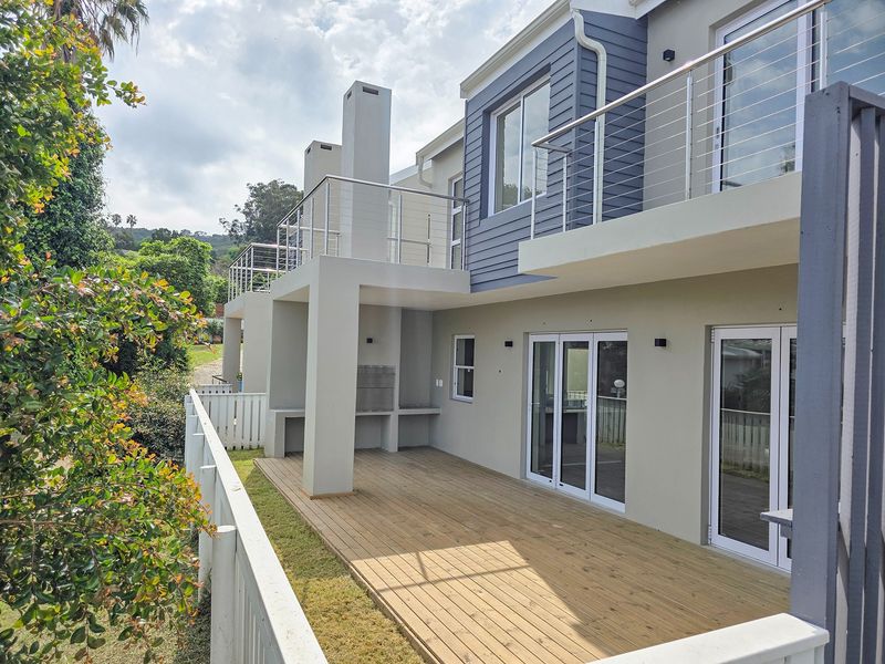 Rear view of the property featuring a spacious timber deck, built-in braai area, and upper-level balcony with modern stainless steel balustrades.