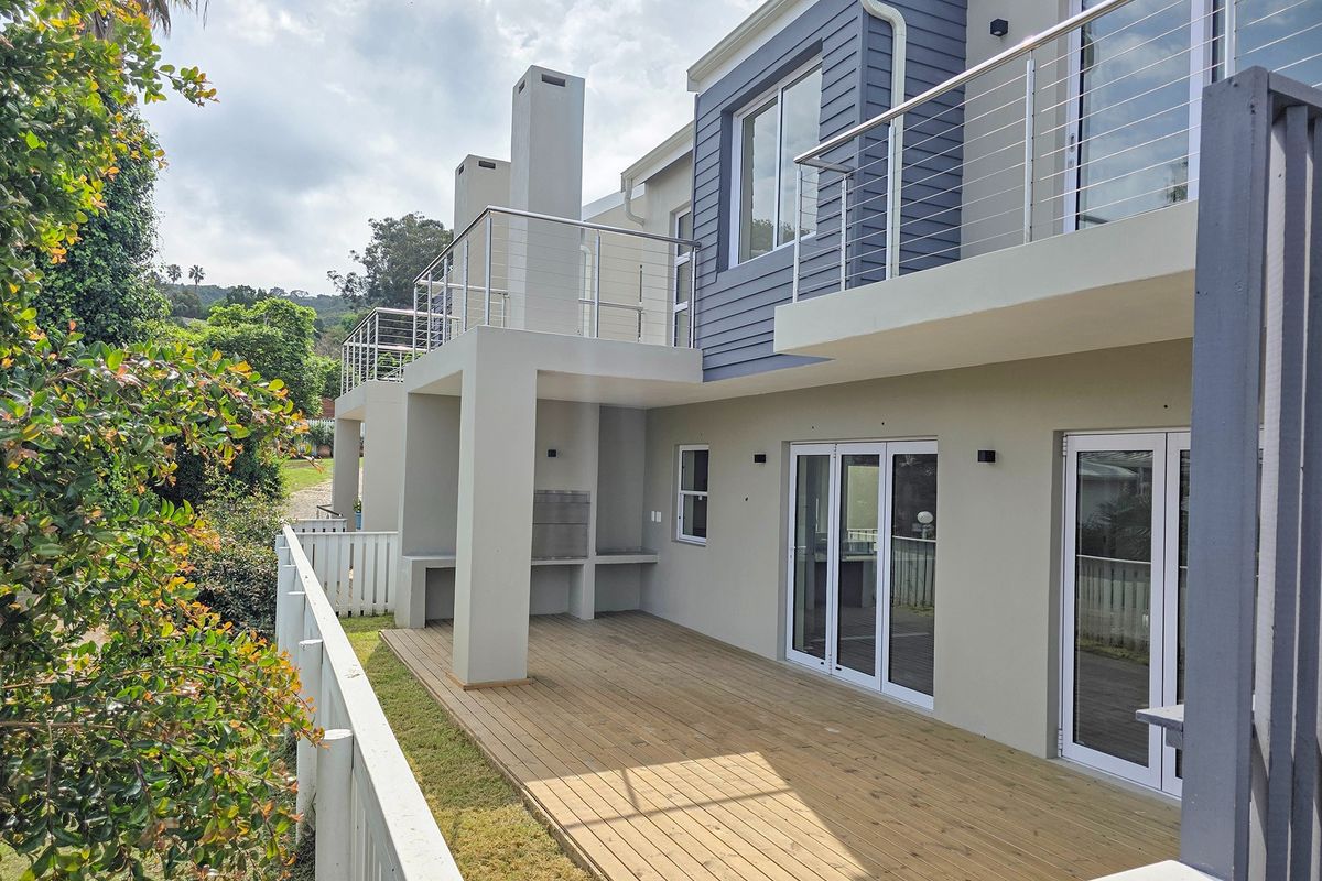 Rear view of the property featuring a spacious timber deck, built-in braai area, and upper-level balcony with modern stainless steel balustrades.