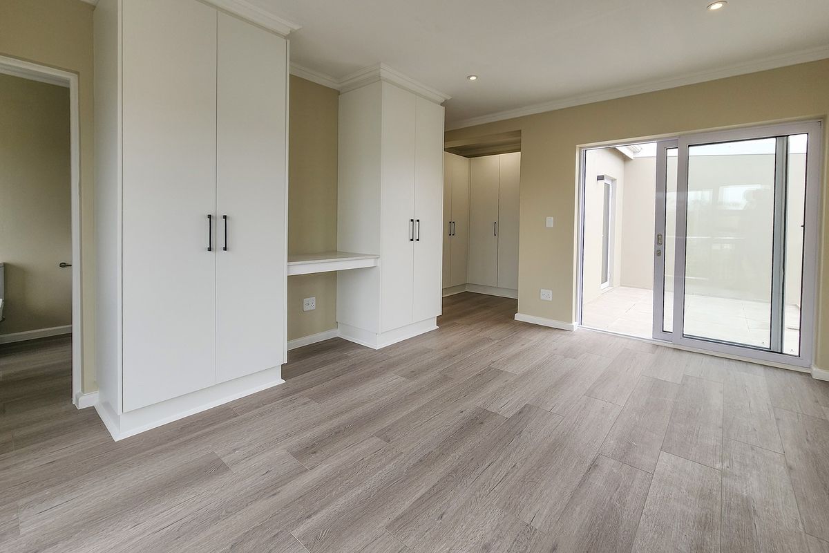 Spacious bedroom featuring modern laminate flooring, extensive built-in cabinetry with an integrated desk, and sliding glass doors leading to an outdoor area.