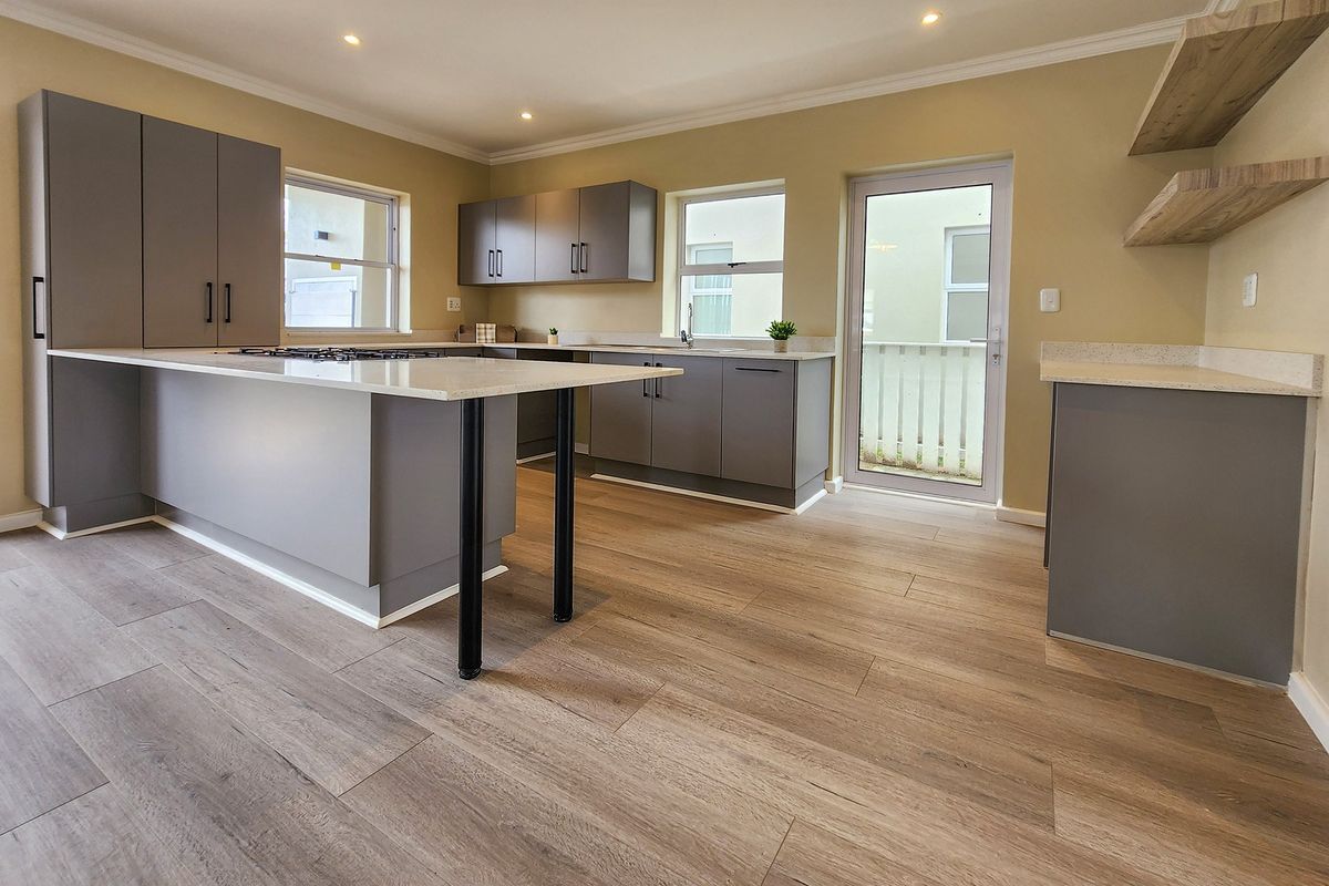 Modern kitchen featuring grey cabinetry, stone countertops, gas cooktop, and light wood-look laminate flooring with direct access to the exterior.
