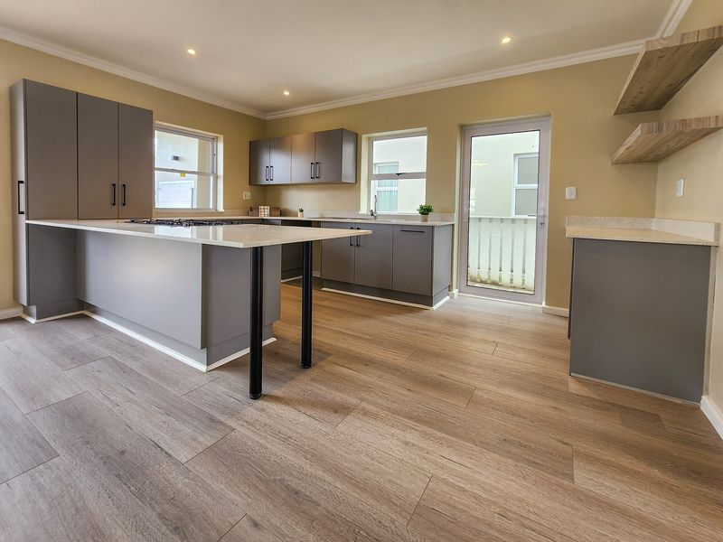 Modern kitchen featuring grey cabinetry, stone countertops, gas cooktop, and light wood-look laminate flooring with direct access to the exterior.