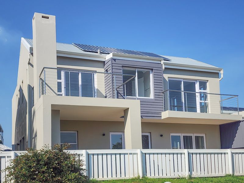 Rear elevation of a modern two-story house featuring balconies with stainless steel balustrades, large sliding doors, and roof-mounted solar panels.