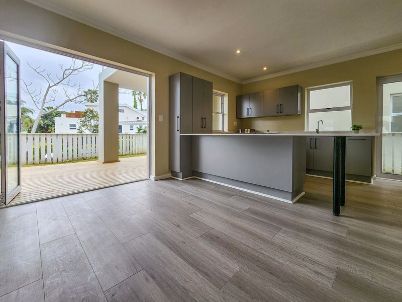 Modern open-plan kitchen with grey cabinetry and island, featuring seamless flow to an outdoor wooden deck through large sliding glass doors.