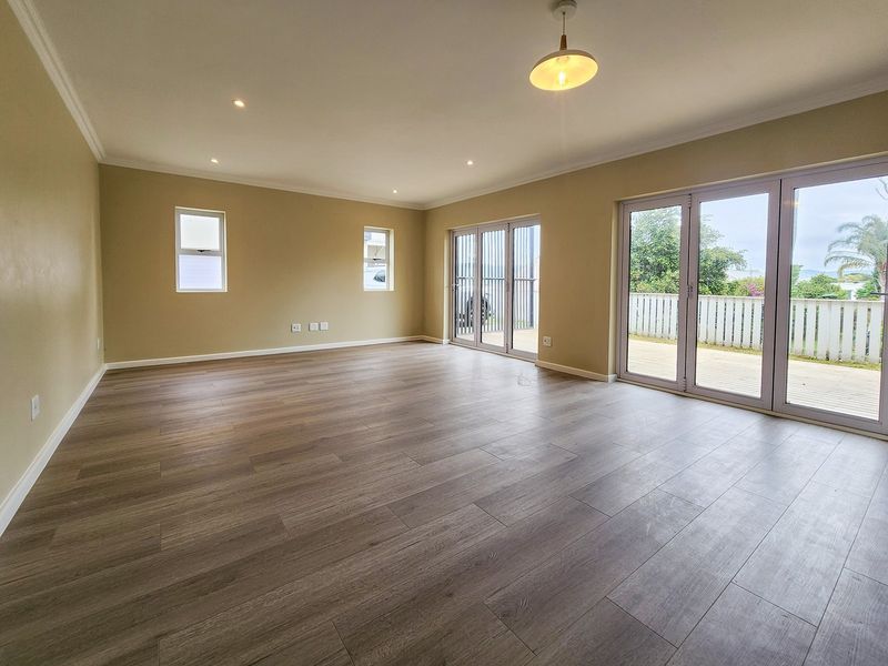 Spacious, light-filled living area featuring modern laminate flooring, recessed lighting, and large aluminium sliding doors providing seamless access to the outdoor deck.
