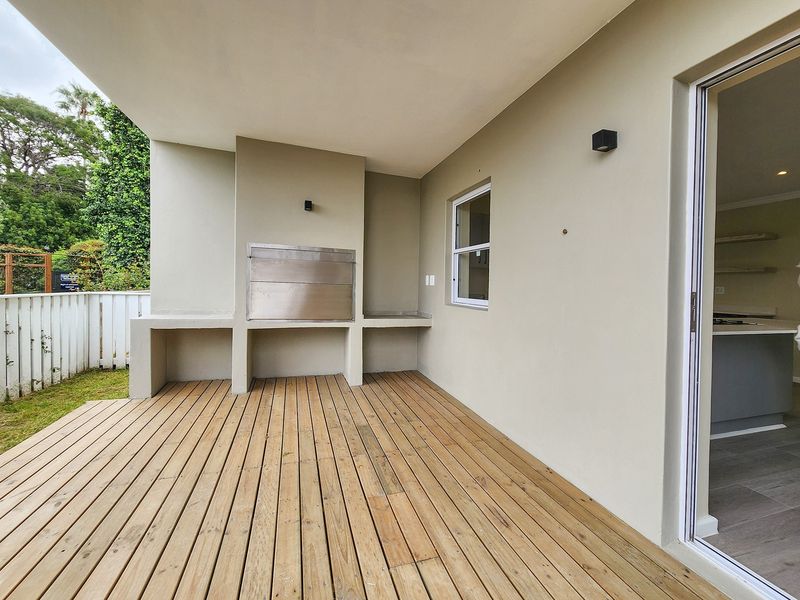 A clean, covered patio featuring timber decking and a built-in stainless steel braai, offering a seamless transition to the garden area.
