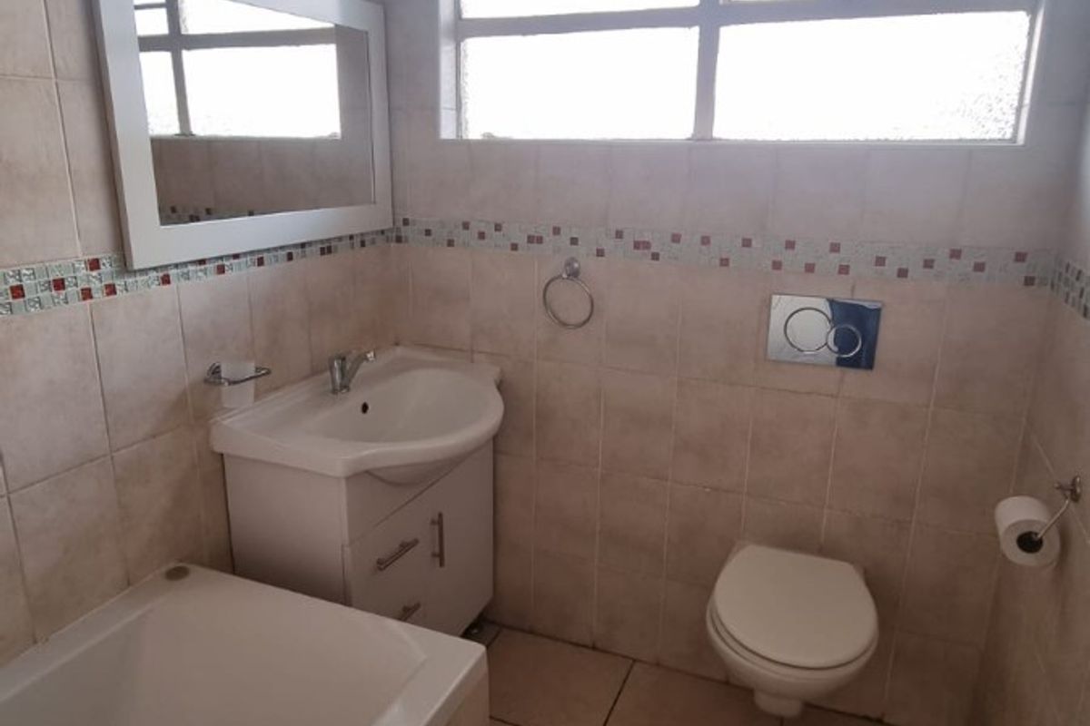 A functional bathroom featuring a bathtub, vanity basin, and wall-mounted toilet with tiled finishes and exposed overhead ducting.