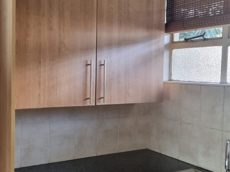 A compact kitchen area featuring wood-look cabinetry, granite countertops, and a stainless steel sink, currently requiring finishing work to the lower wall section.