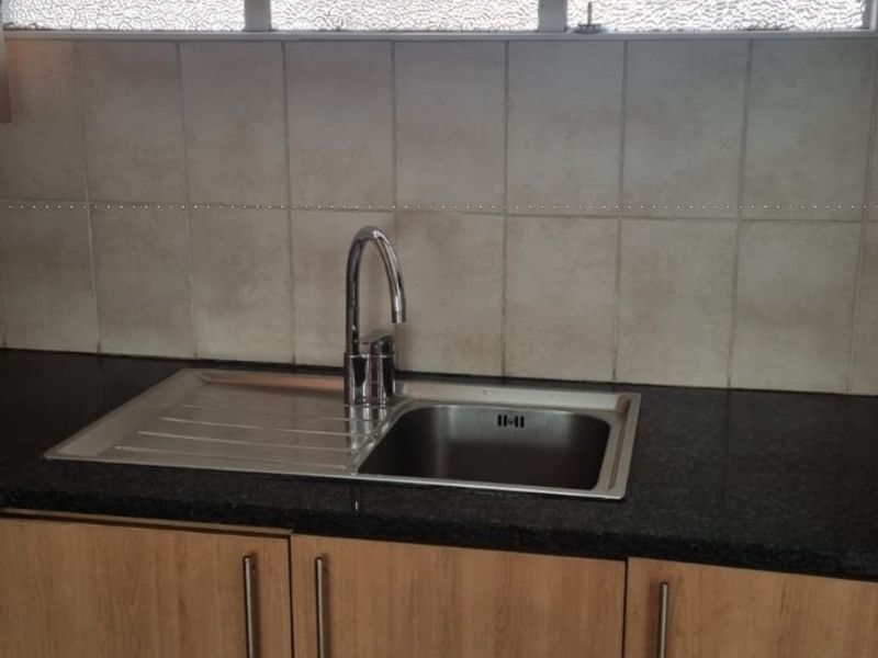 A functional kitchen area featuring a stainless steel sink, granite countertops, light wood-finish cabinetry, and a tiled backsplash under a window.