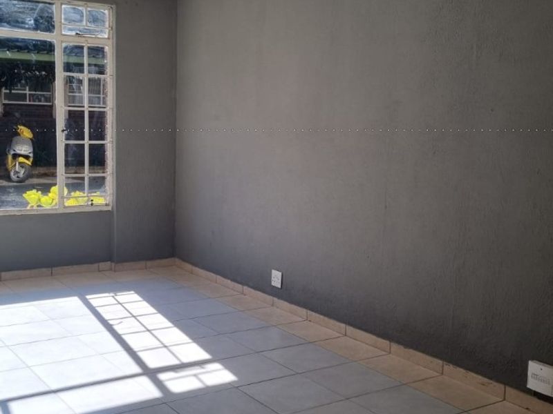 An empty living room featuring neutral tiled flooring, dark grey painted walls, and a large multi-pane window allowing for natural light.