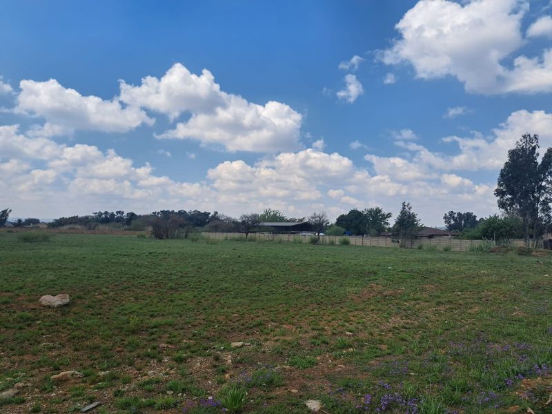 A wide-angle view of a vacant residential plot featuring open grass land and perimeter boundary fencing.