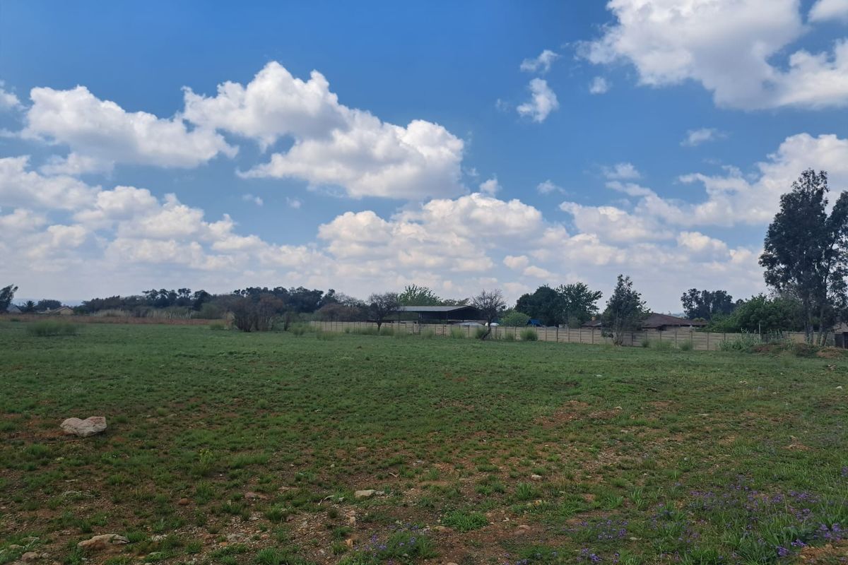 A wide-angle view of a vacant residential plot featuring open grass land and perimeter boundary fencing.