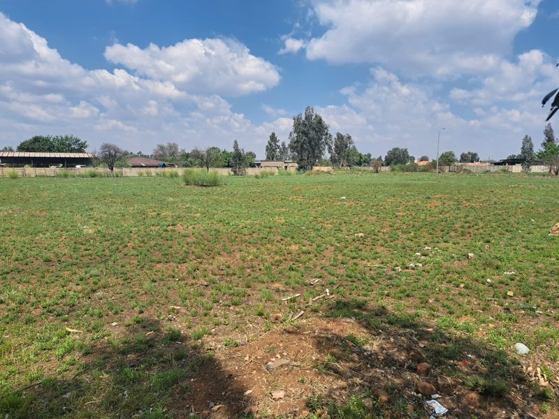 A wide, open residential vacant land plot featuring natural grass coverage and perimeter walling, suitable for future development.