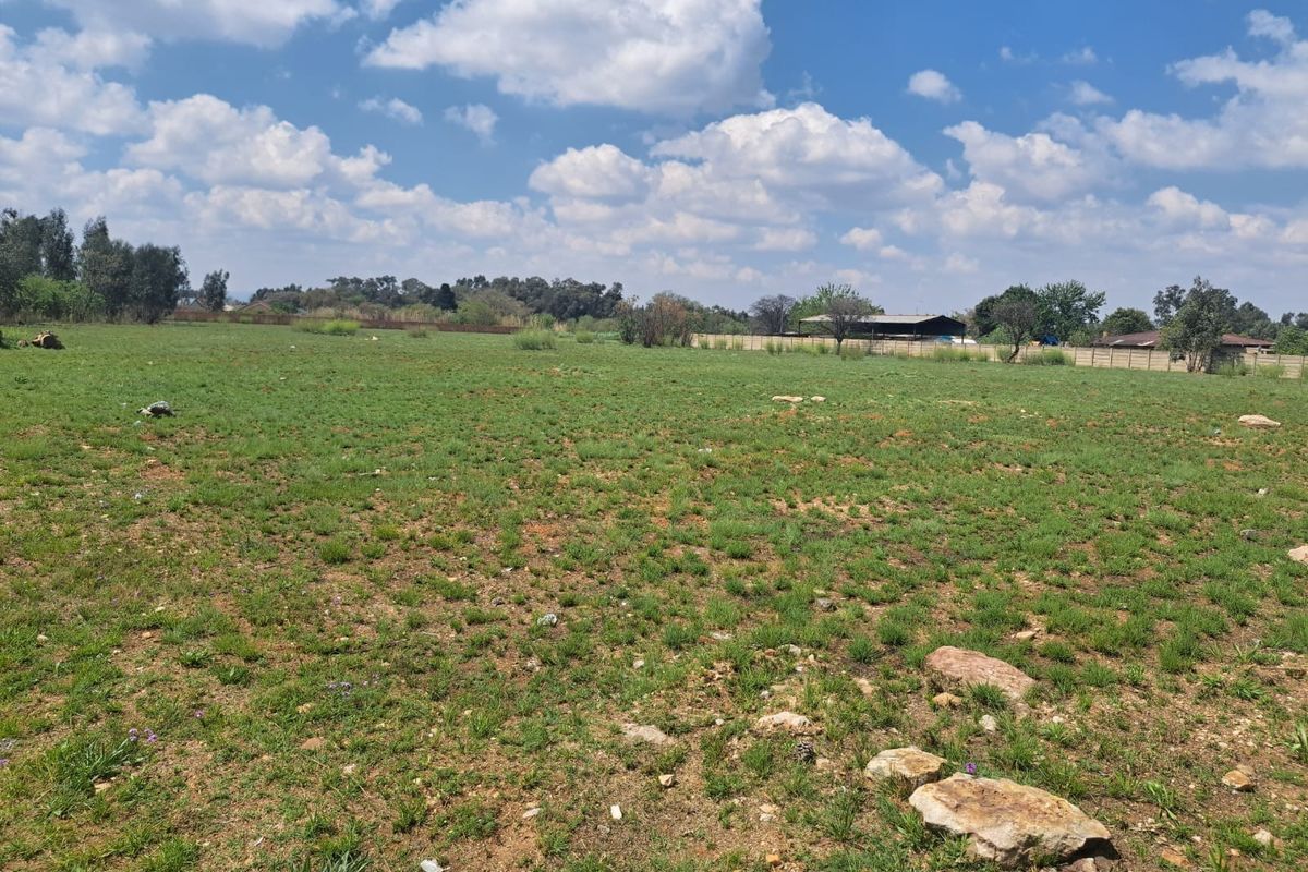 A wide-angle view of a vacant residential plot featuring open grassland and perimeter boundary walls under a clear blue sky.