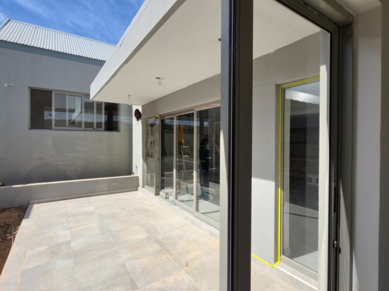 A modern, newly constructed patio area featuring large sliding glass doors, tiled flooring, and recessed lighting, currently awaiting final landscaping completion.