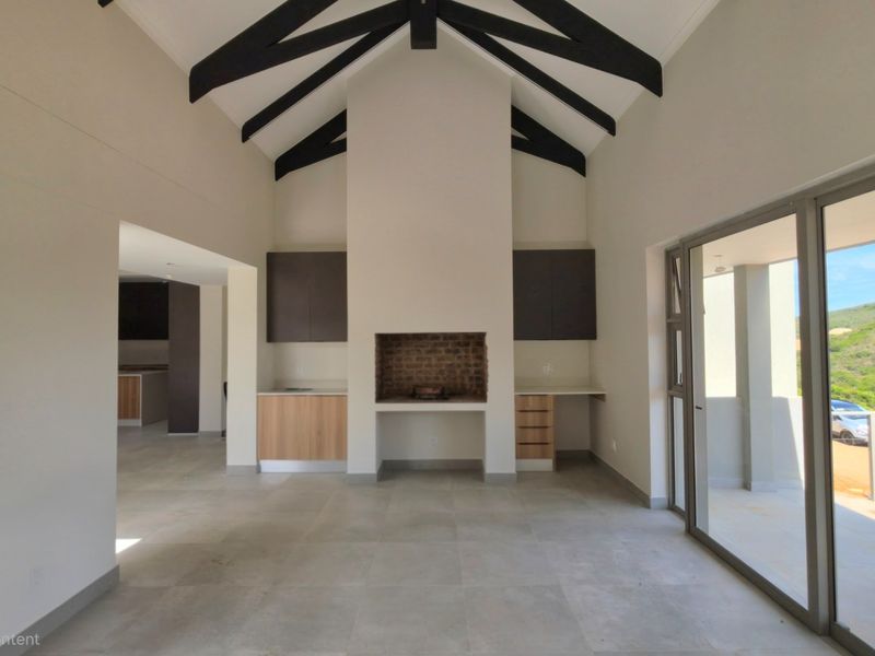 Spacious living area featuring a vaulted ceiling with exposed beams, built-in fireplace, tiled floors, and large sliding doors opening to an outdoor patio.