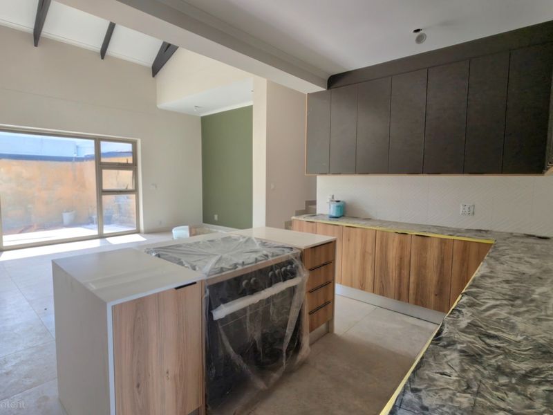 Modern open-plan kitchen and living area featuring vaulted ceilings, exposed rafters, contemporary cabinetry, stone countertops, and large sliding doors leading to the rear yard.