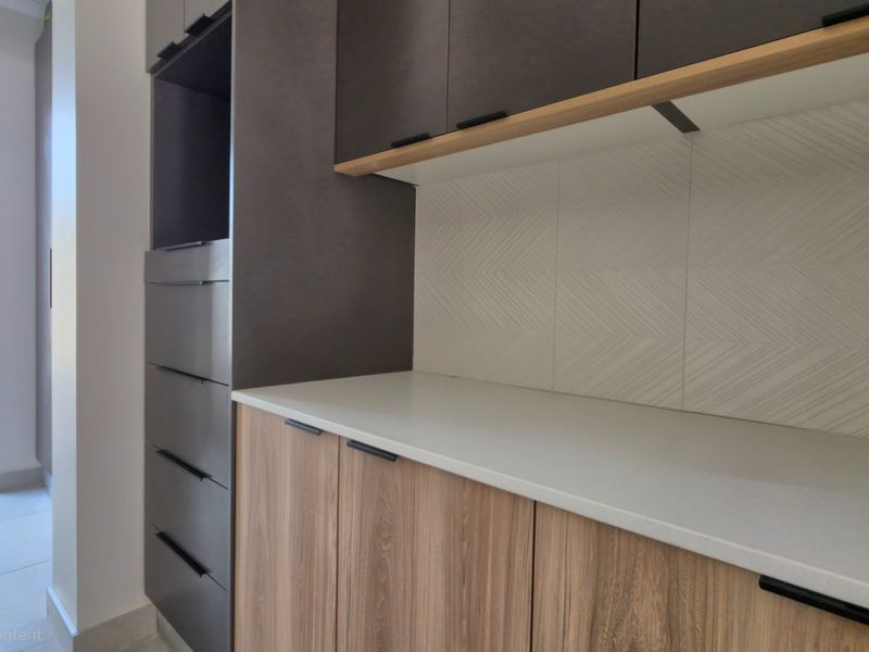 A modern scullery or utility area featuring sleek dark and wood-grain cabinetry, stone countertops, and a stylish herringbone backsplash.